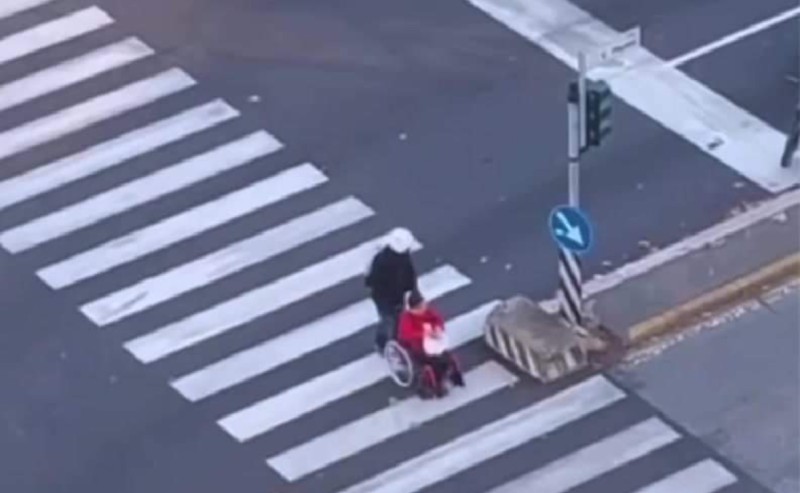 Sesto, un uomo arresta lo scooter ad un semaforo ed aiuta una donna in carrozzina ad attraversare la strada.